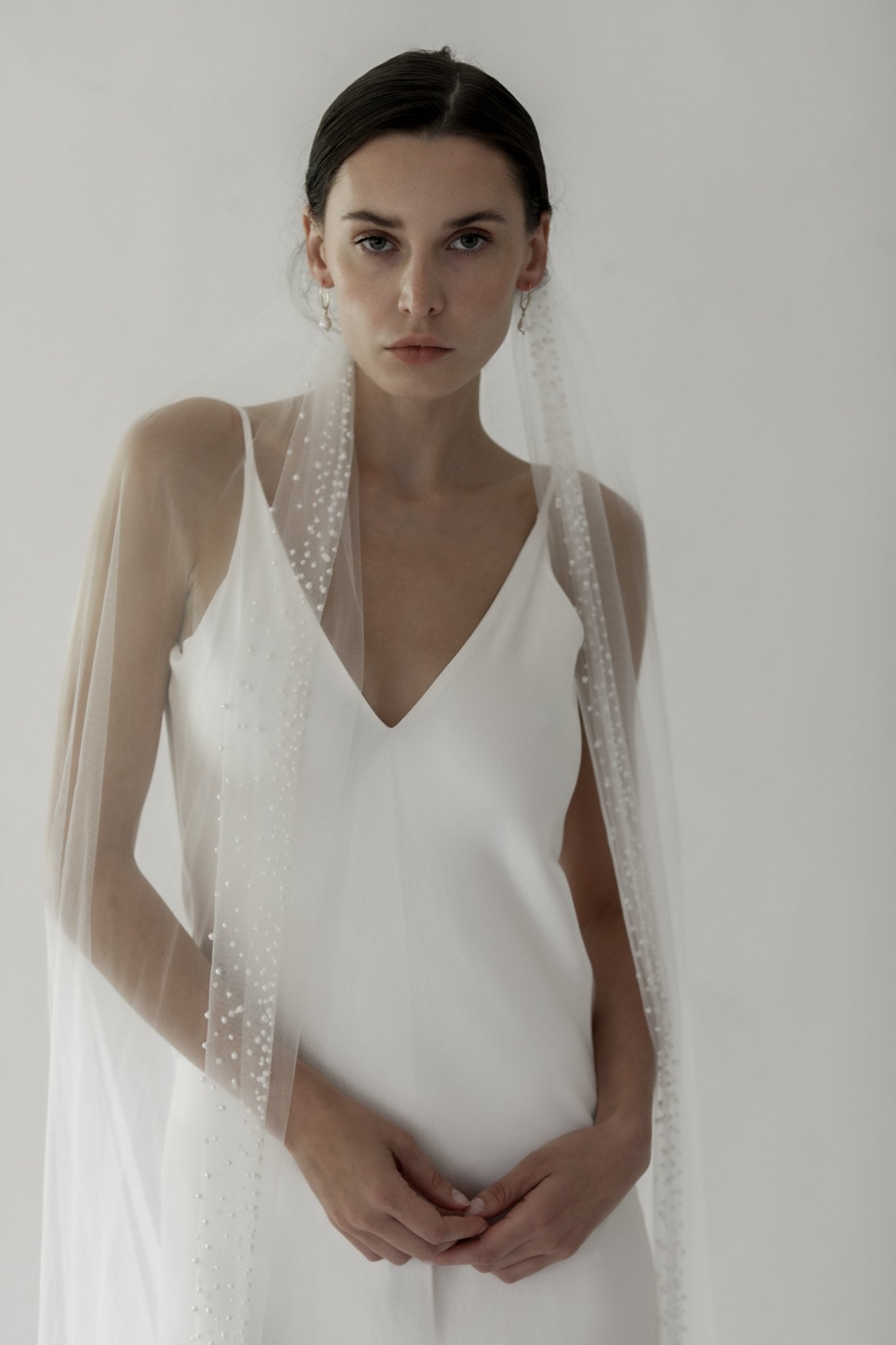 Brunette bride wearing Hayden Pearl edge bridal veil by AB Ellie with sheath wedding dress on white background