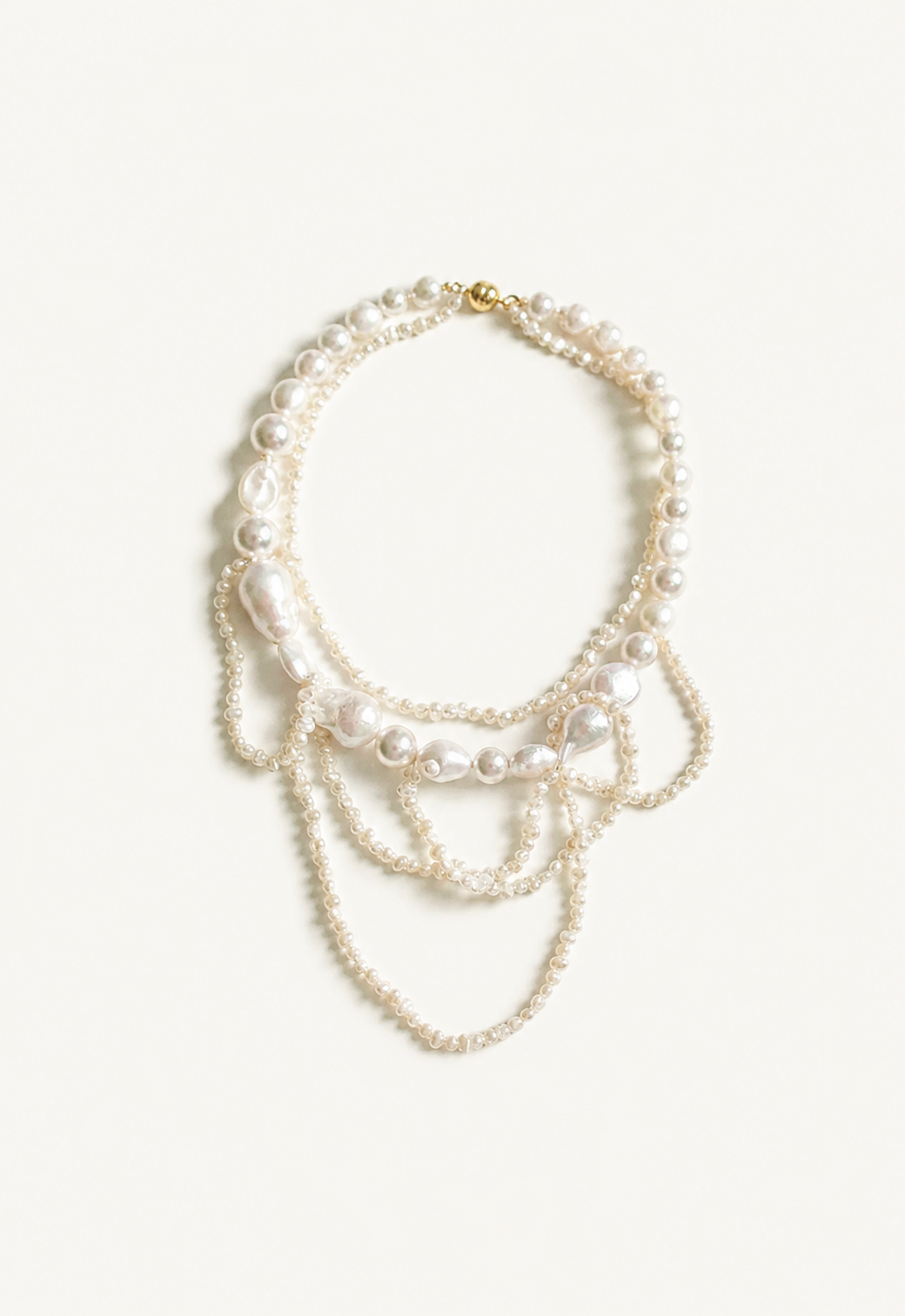 A multi-strand freshwater pearl necklace with baroque pearls and a gold clasp, displayed on a clean, light off-white background.
