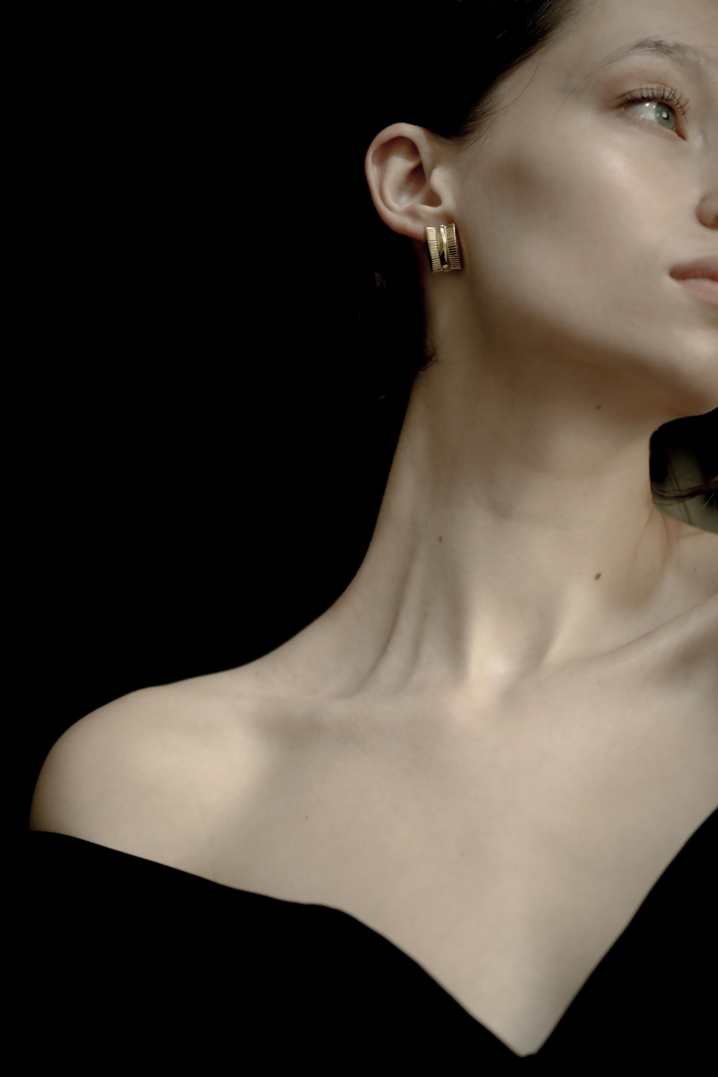 Close-up of a woman wearing AB Ellie gold channel sterling silver hoop earrings against a black background