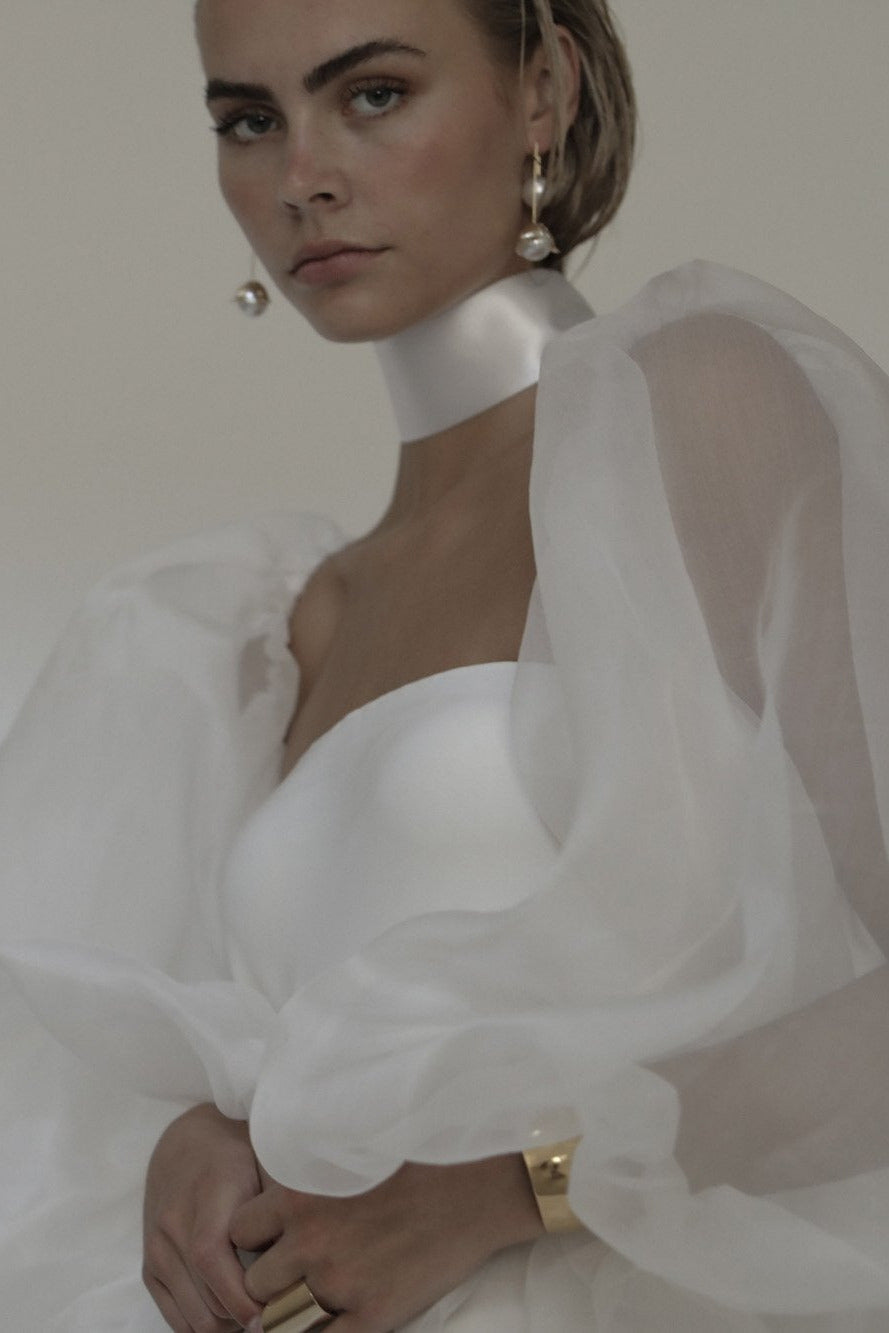 Front view of blonde bride wearing the Bardot pearl drop earrings by AB Ellie paired with statement bridal sleaves