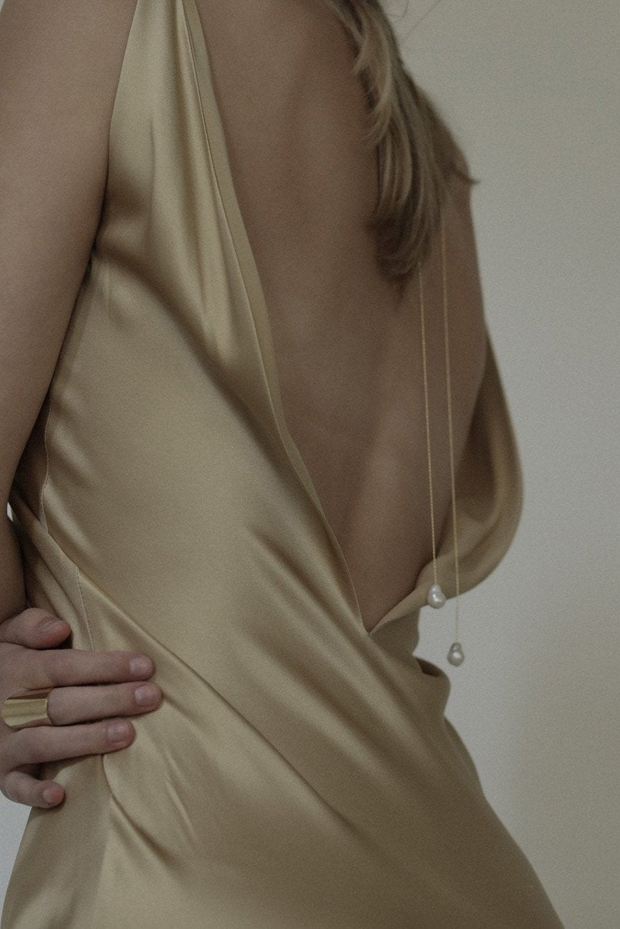 Back view of woman wearing gold, open-back dress with the baroque pearl wrap lariat necklace