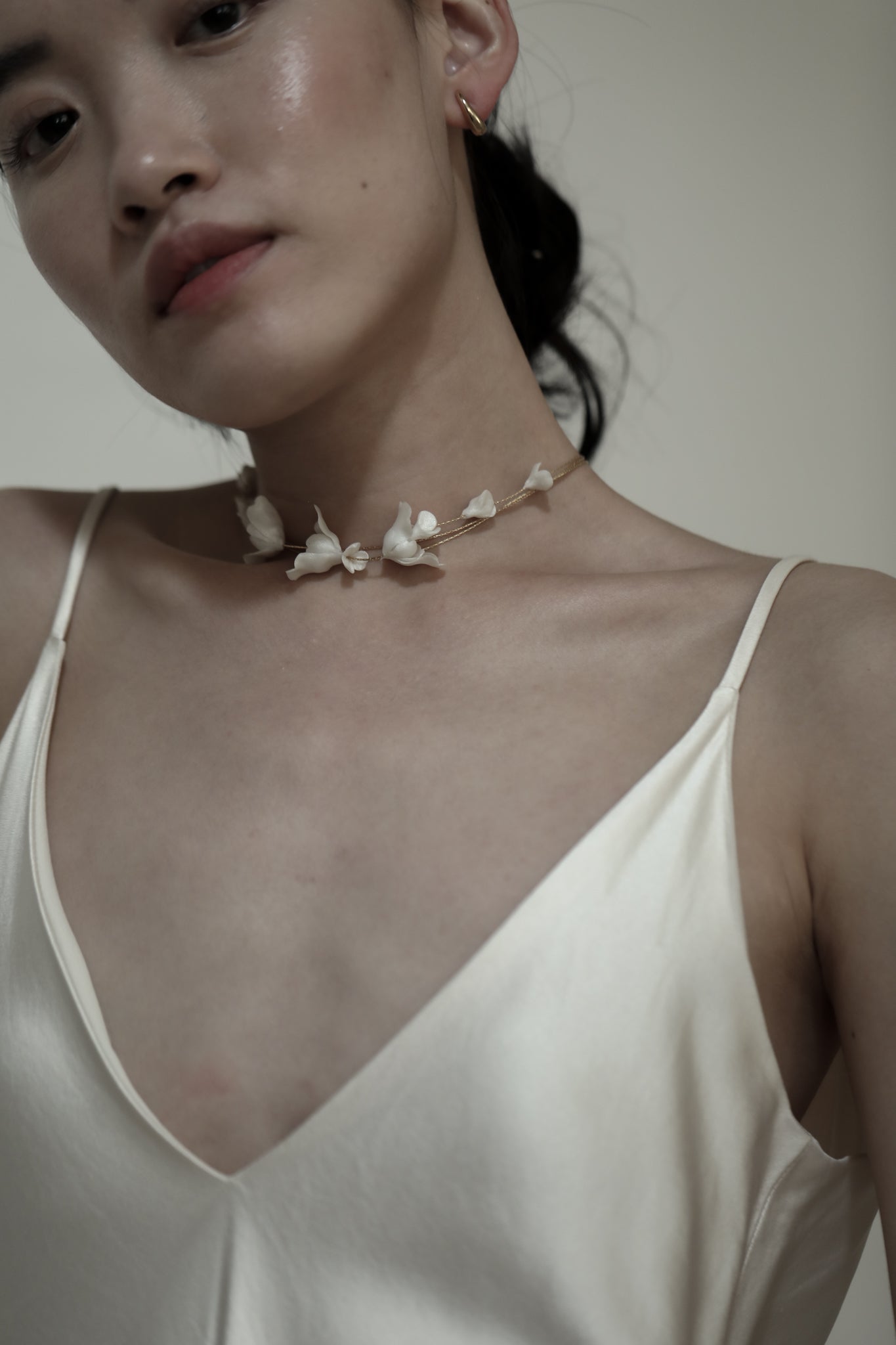 Bride wearing a delicate ivory floral necklace with a simple wedding gown on a white background