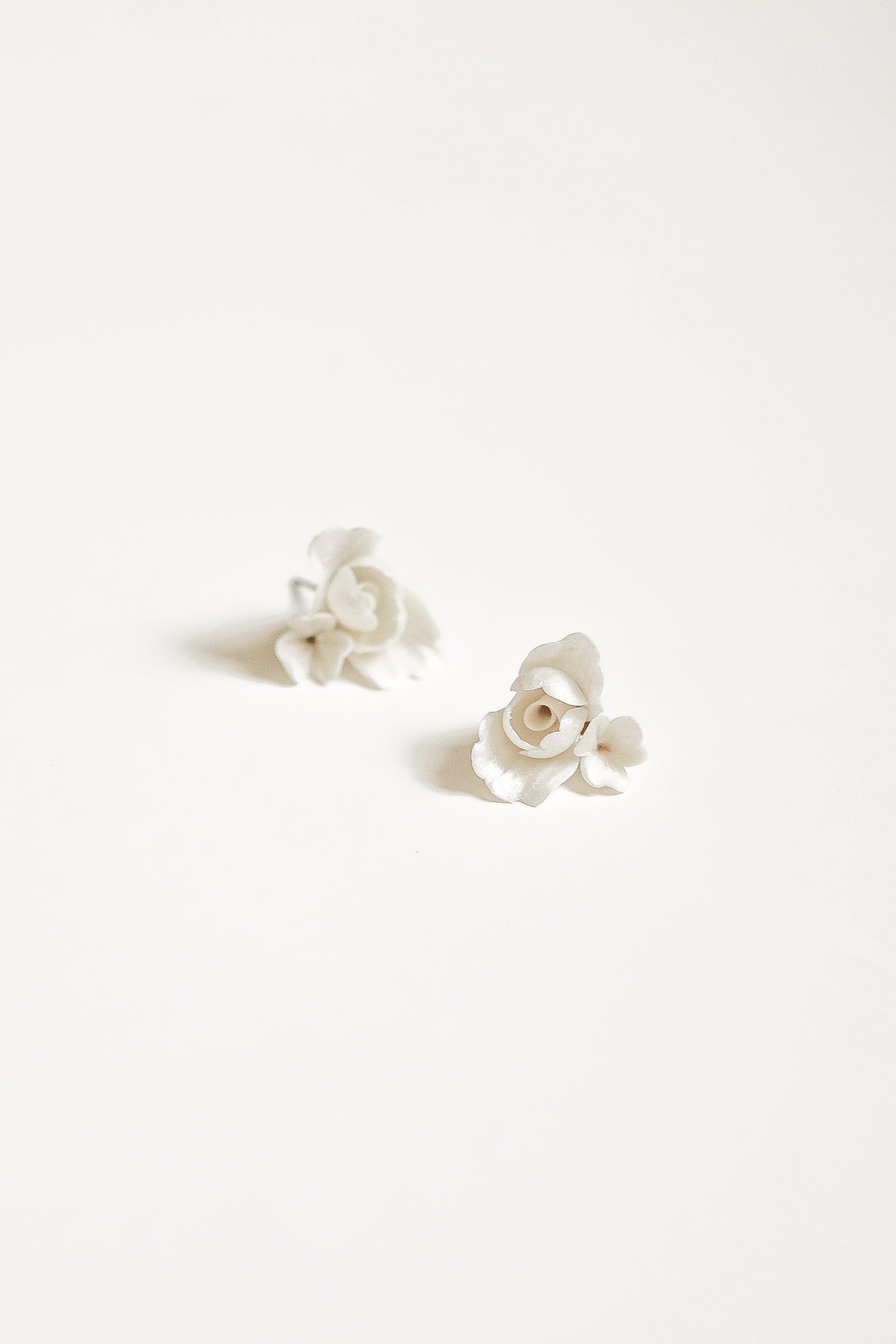 A pair of ivory colored floral stud earrings by AB Ellie set against a white background.
