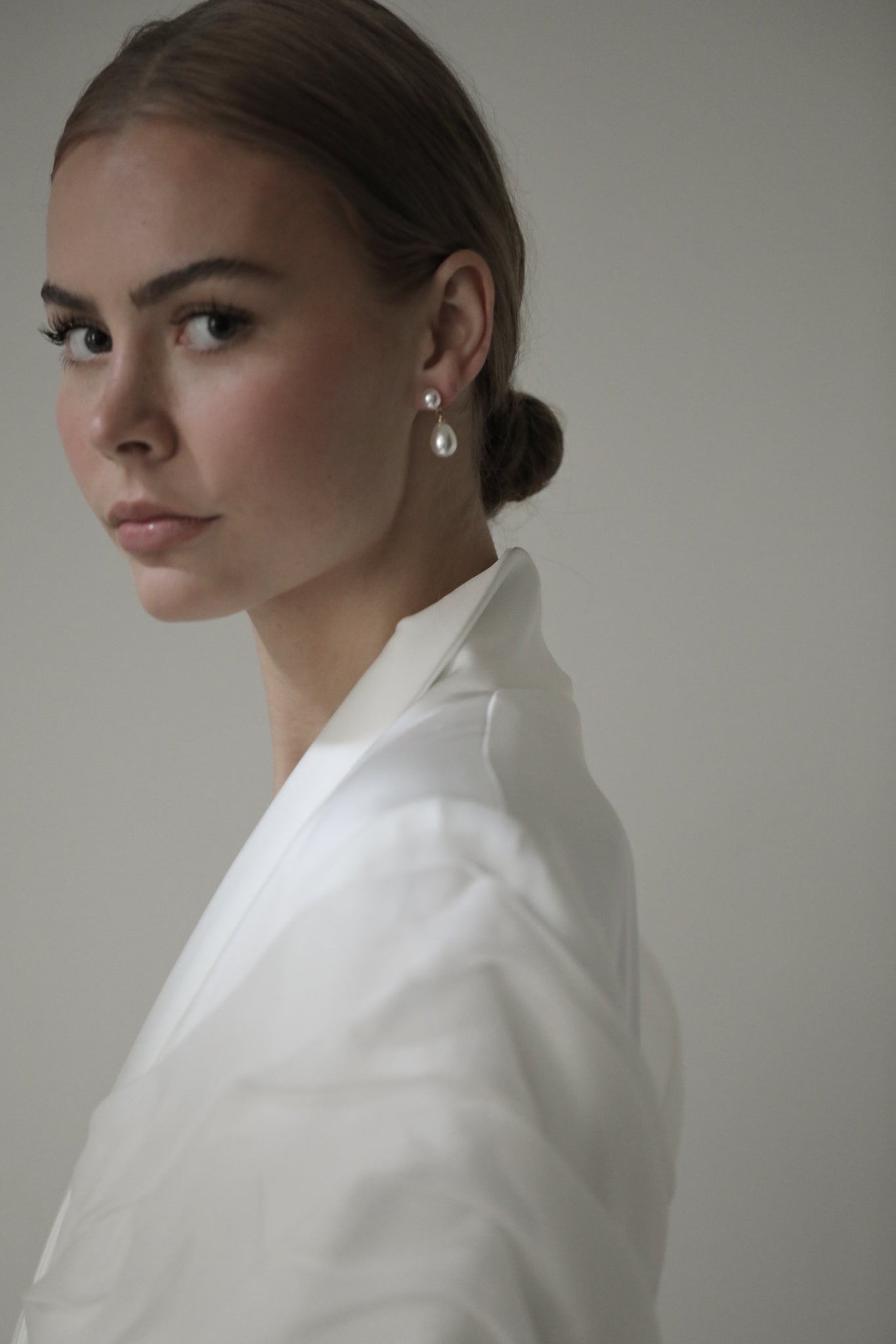 Brunette model wearing bridal suite coat with double pearl earrings with hair in bun