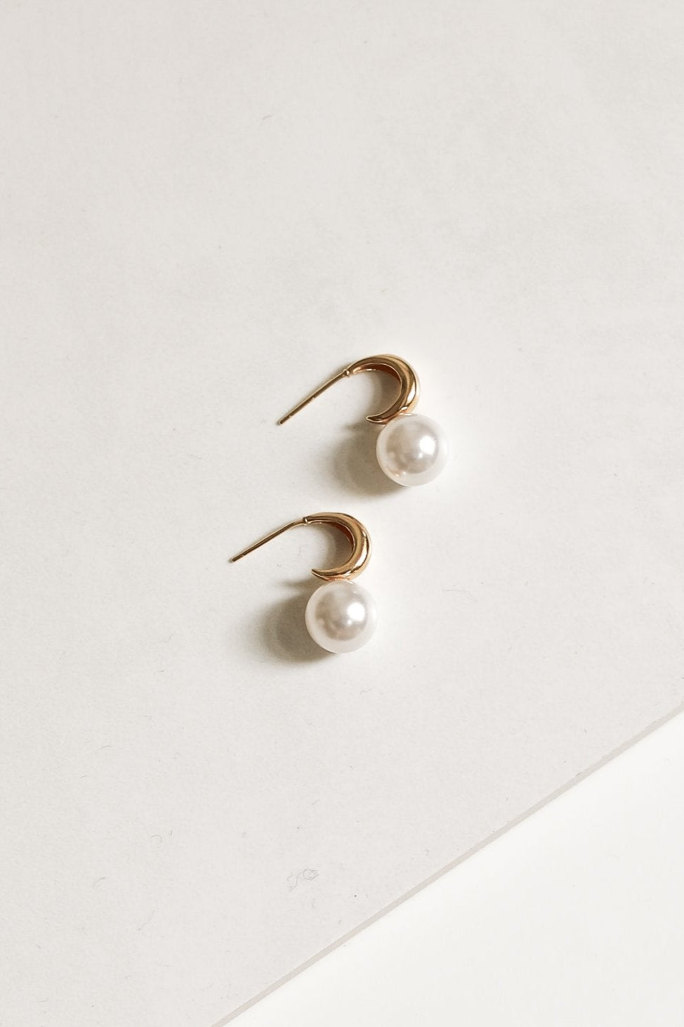 Pair of gold crescent hoop pearl earrings by AB Ellie on white background