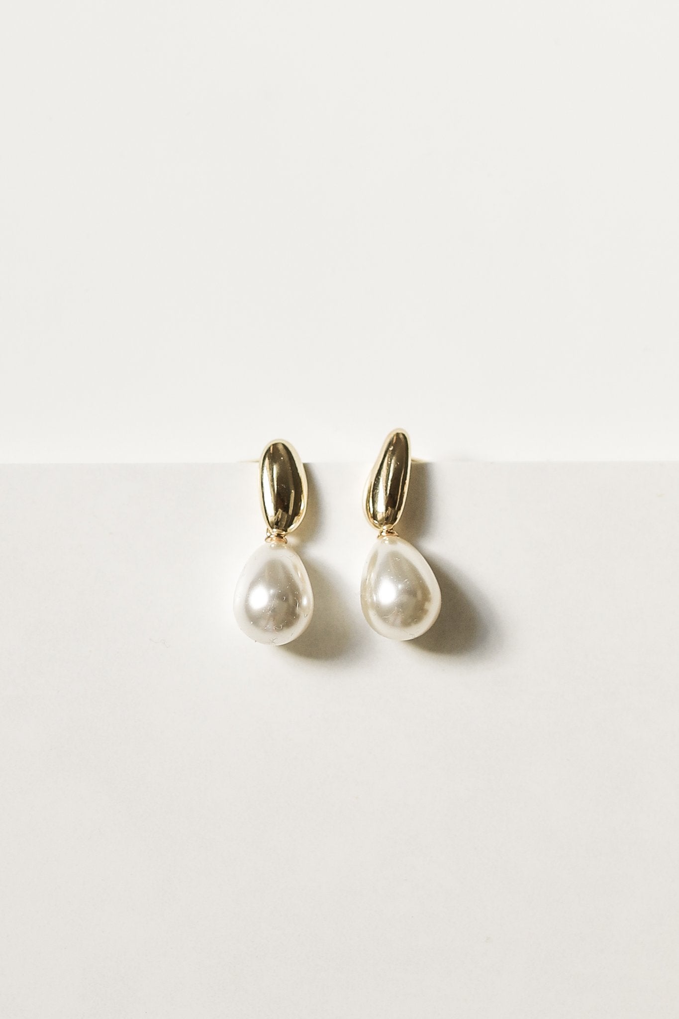 Pair of gold pearl drop earrings by AB Ellie on white background