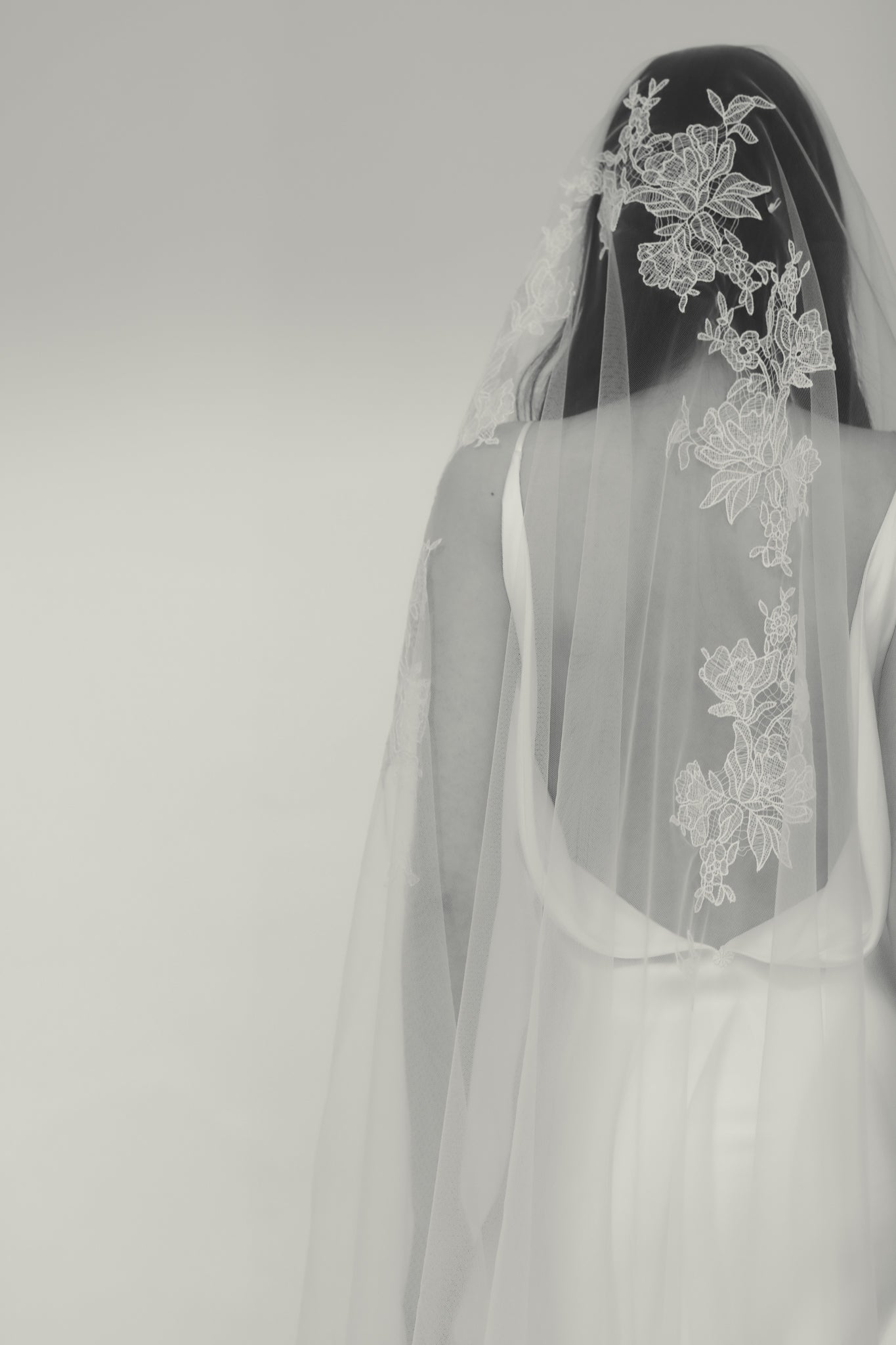Back view of bride wearing wedding veil with floral lace details on a white background