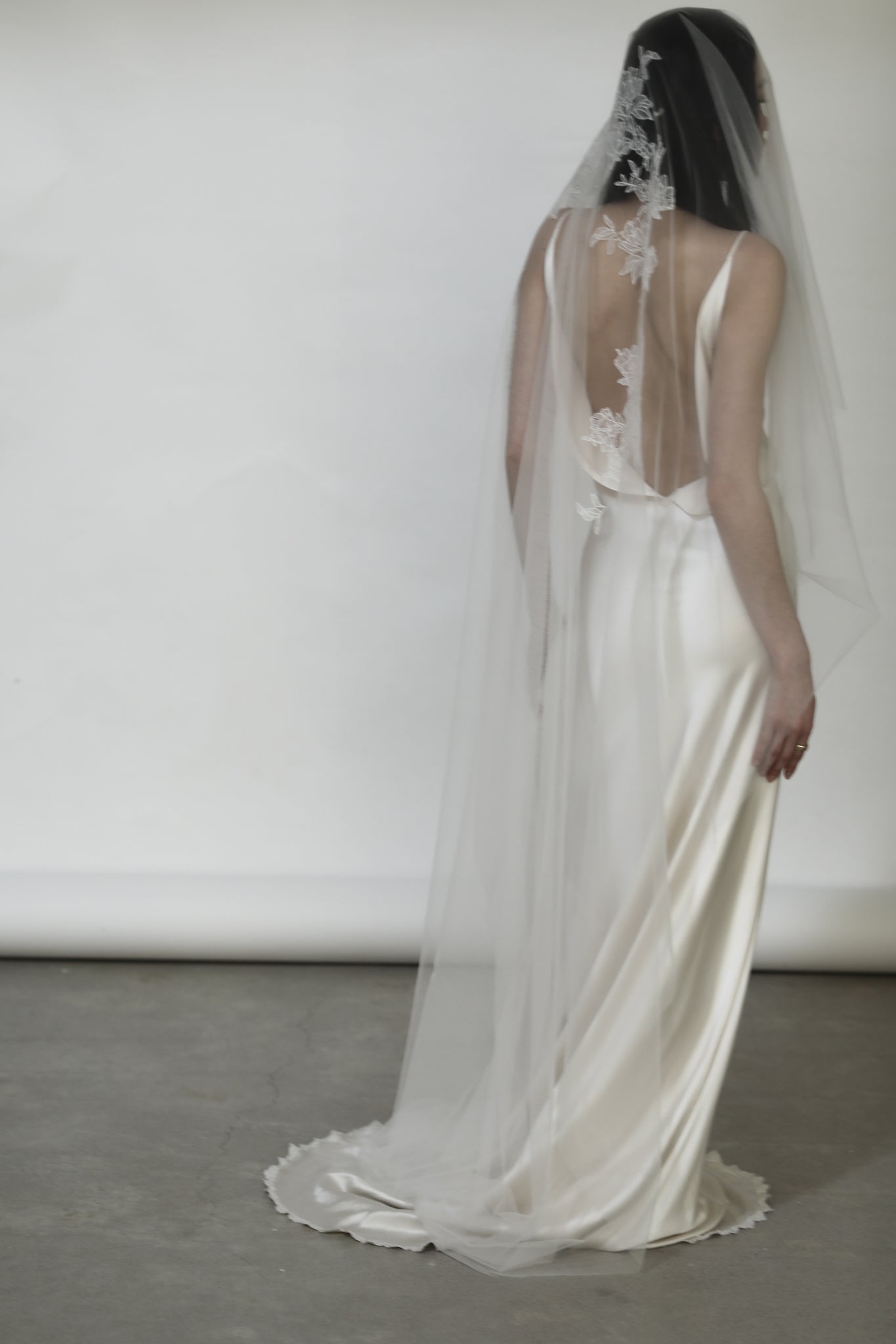 Back view of bride wearing silk wedding dress with lace detailed veil and a long train on a white background