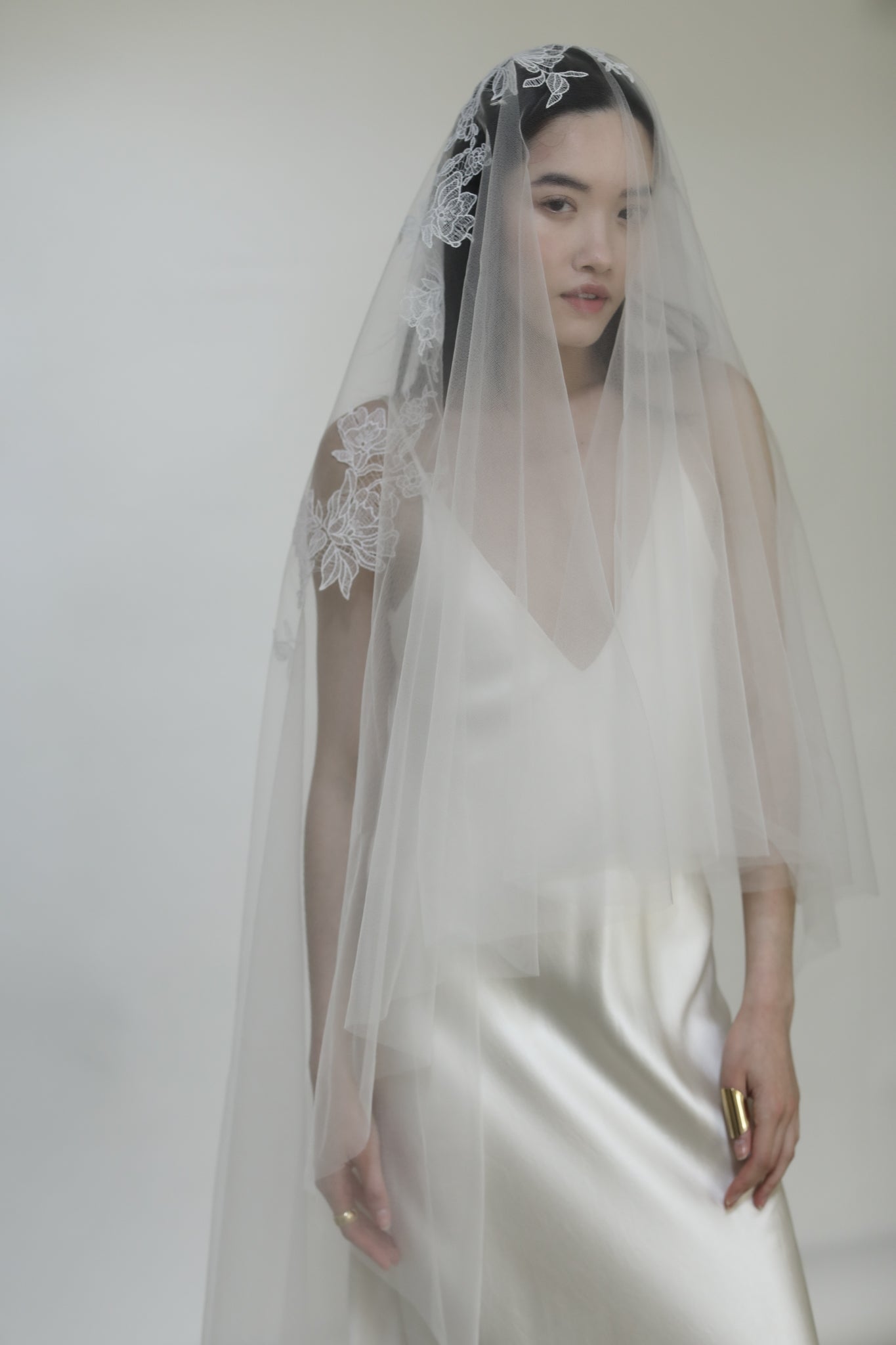 Bride wearing a silk wedding dress with a lace bridal veil against a white background