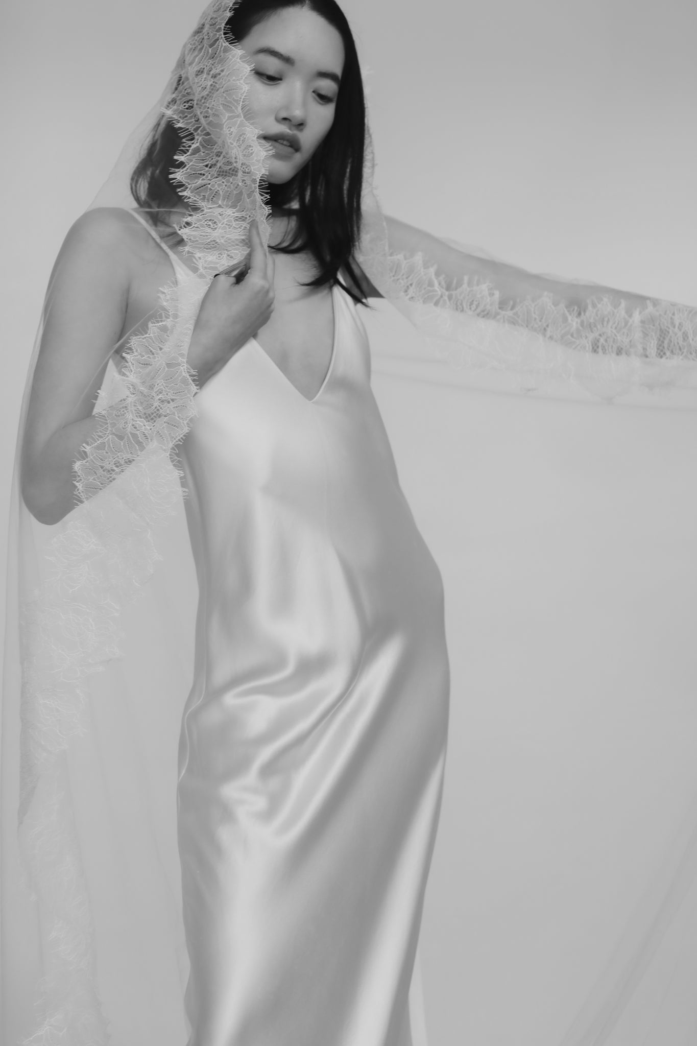 Bride wearing a white satin slip wedding dress with lace detailed bridal veil against a white background