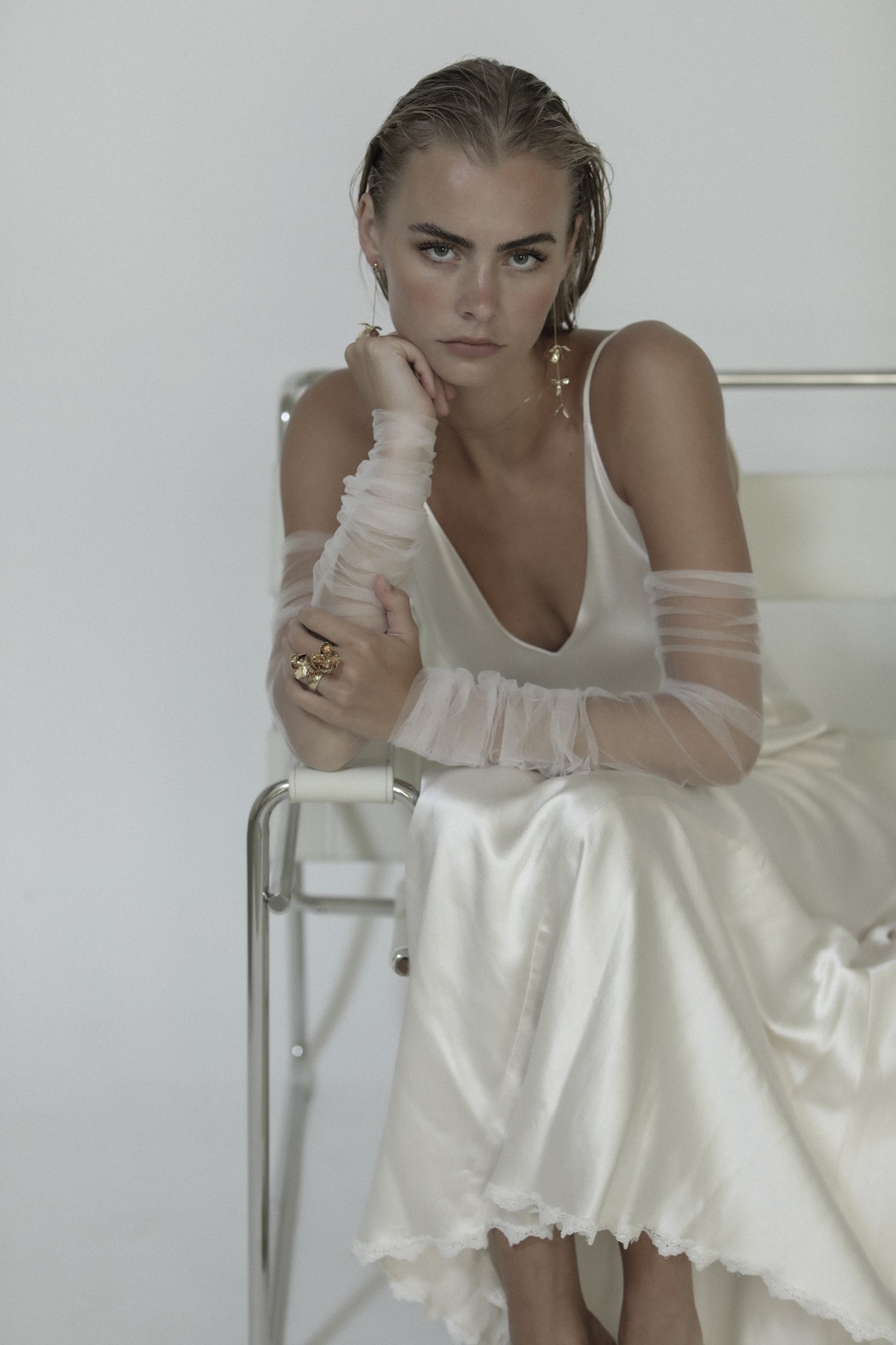 Blonde bride sitting wearing gold Magnolia strand earrings paired with a sheath wedding dress