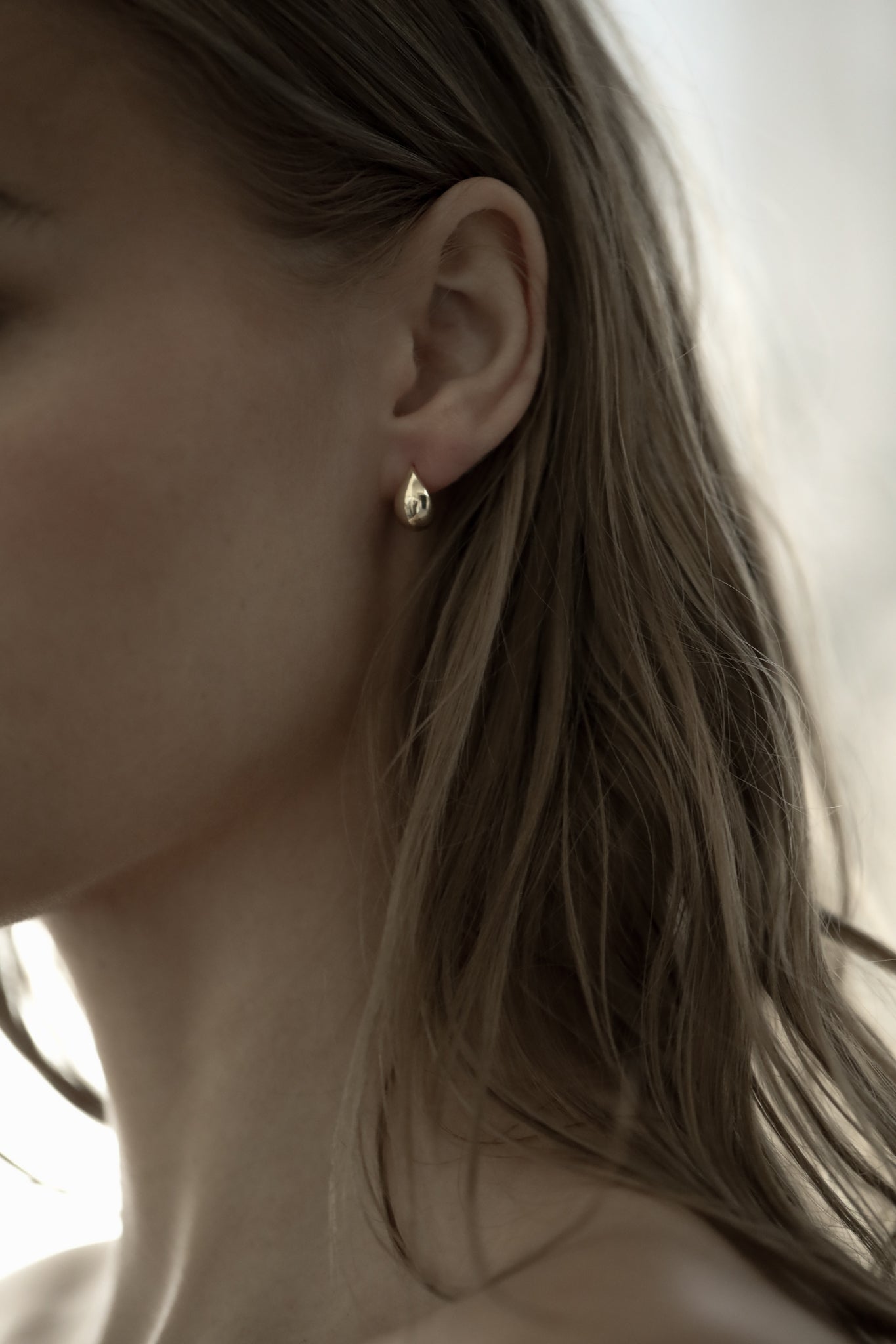 A close-up photo of a woman wearing a the gold micro orb earring by AB Ellie.