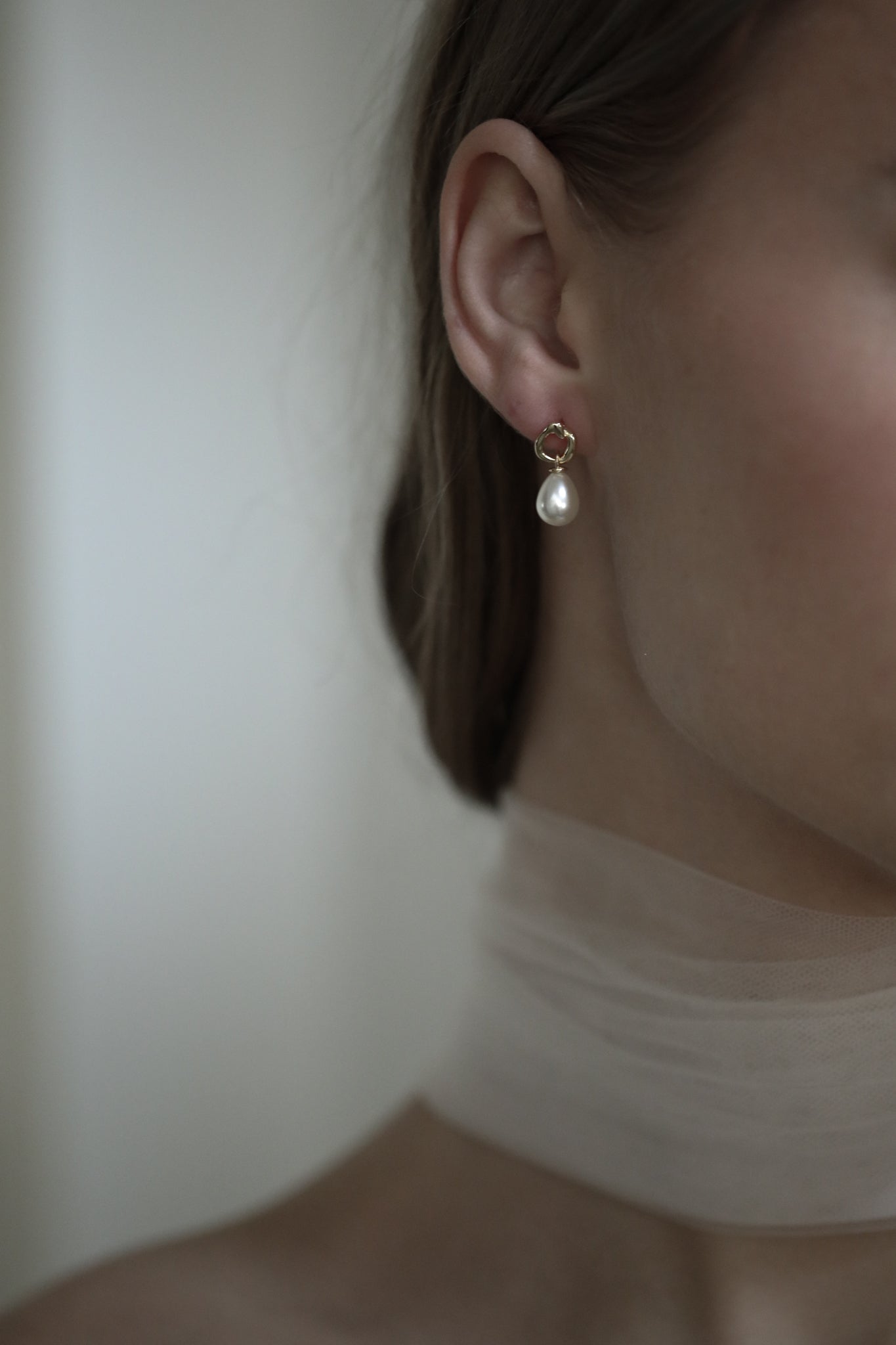 Close up side view of bride wearing the mini gilded pearl drop earrings paired with silk bridal scarf