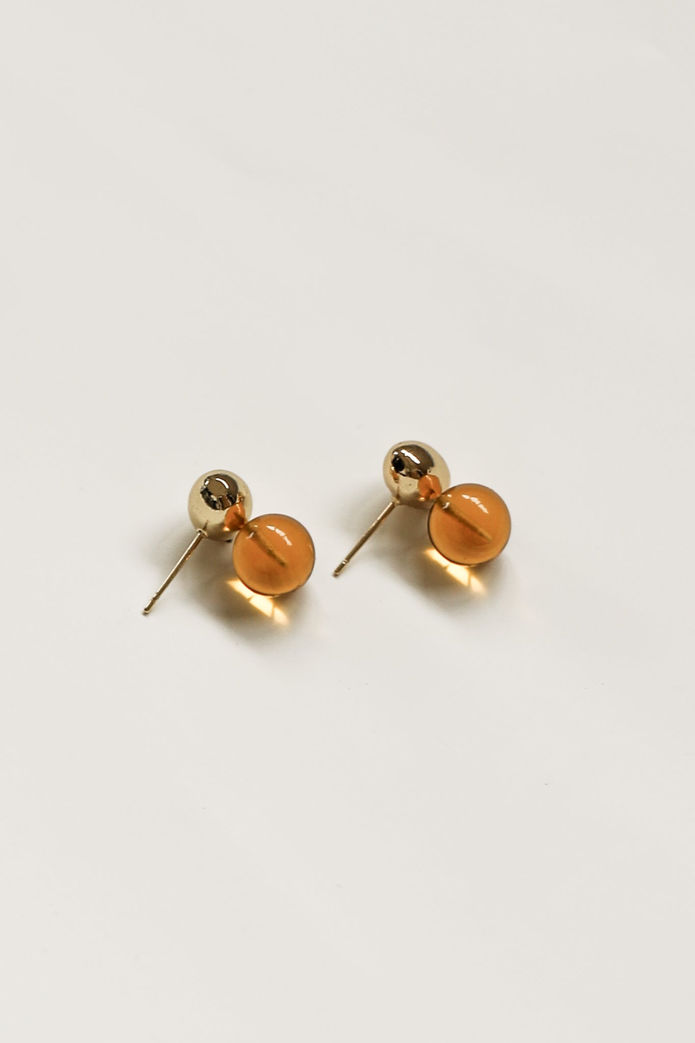 Flat image of gold orb and amber glass drop earring by A.B. Ellie on white background