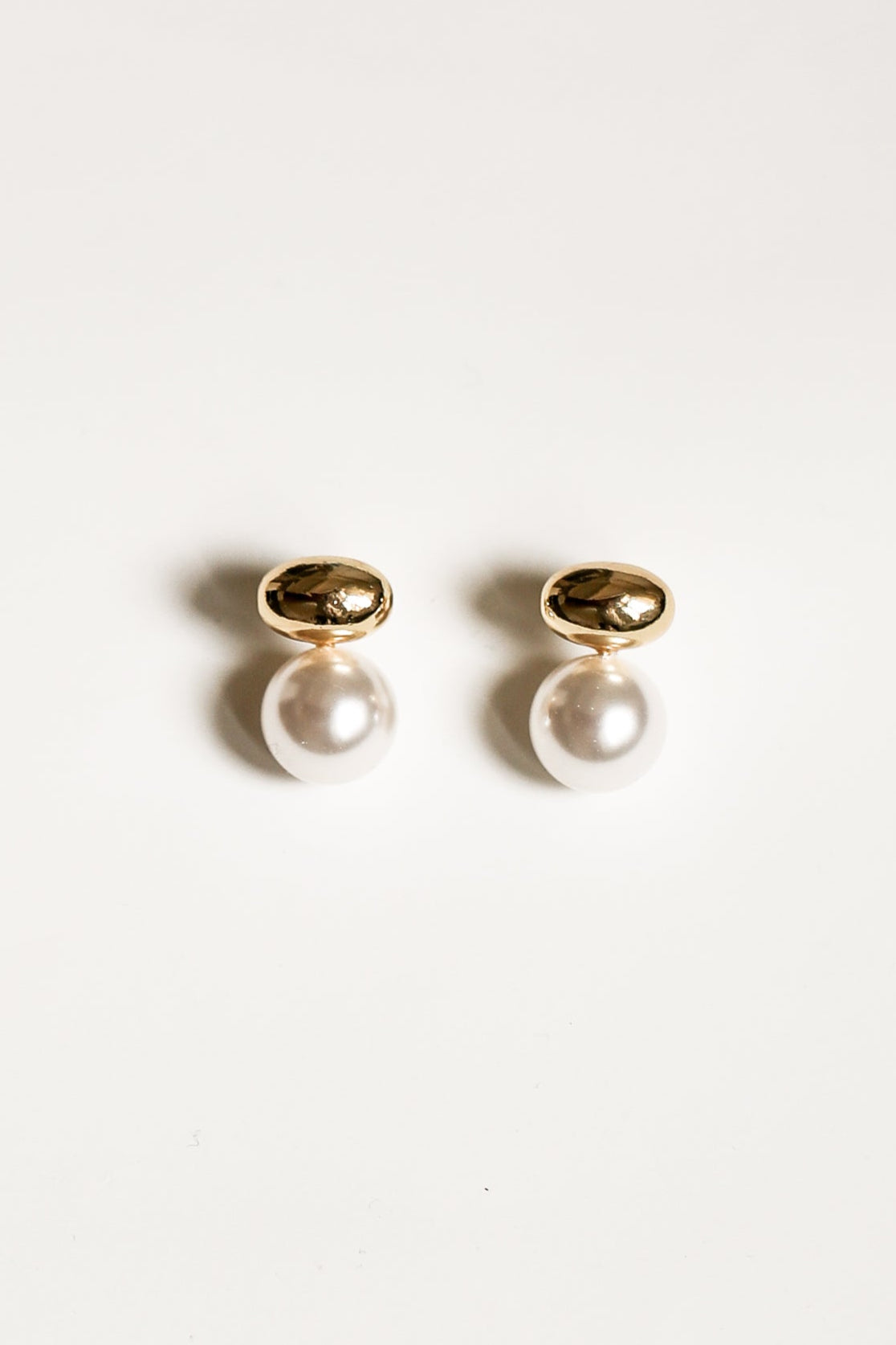 A pair of gold orb and pearl drop earrings by AB Ellie on a white background