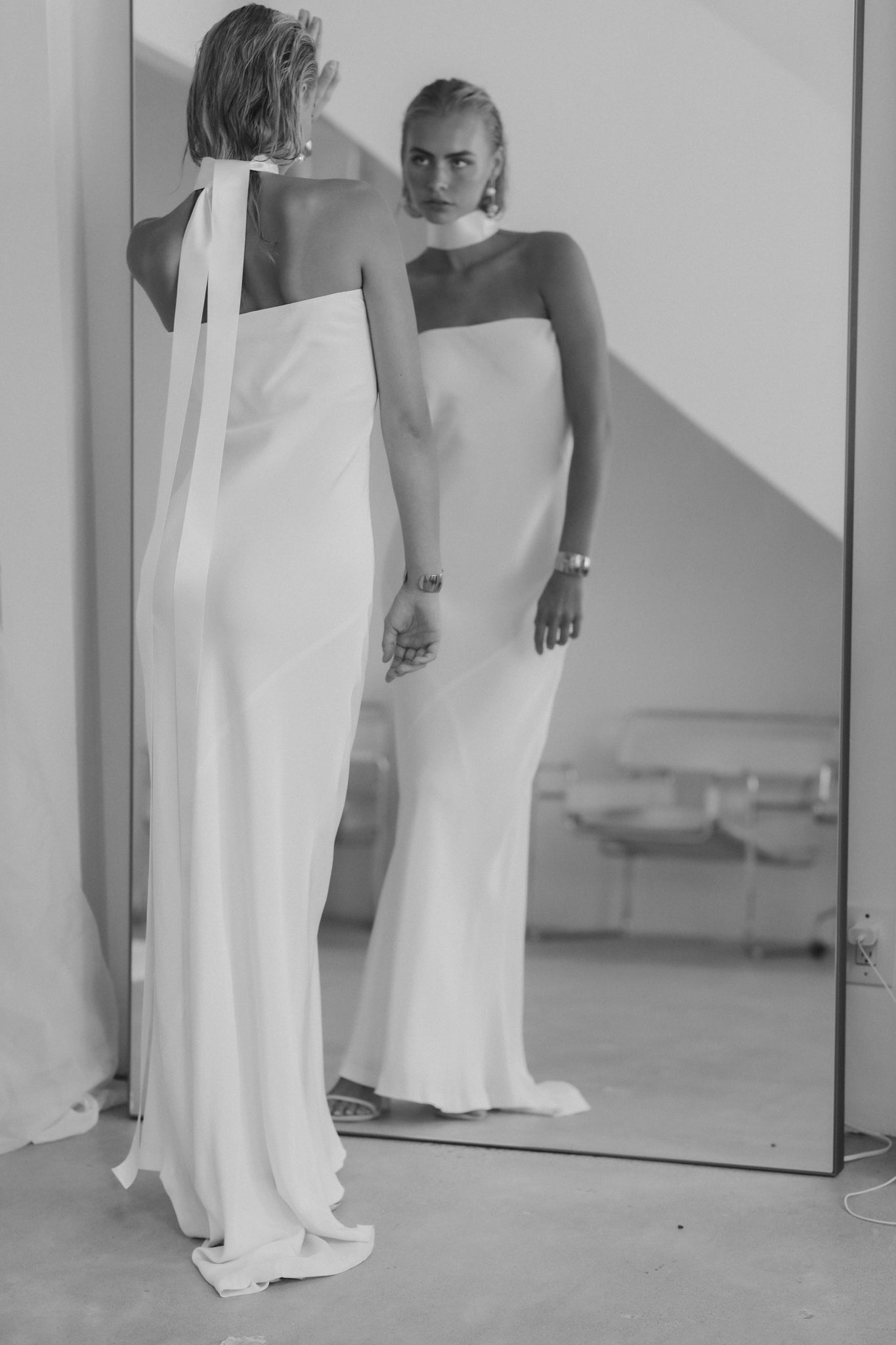 Black and white image of bride wearing strapless wedding dress paired with satin necktie and gold with pearl earrings