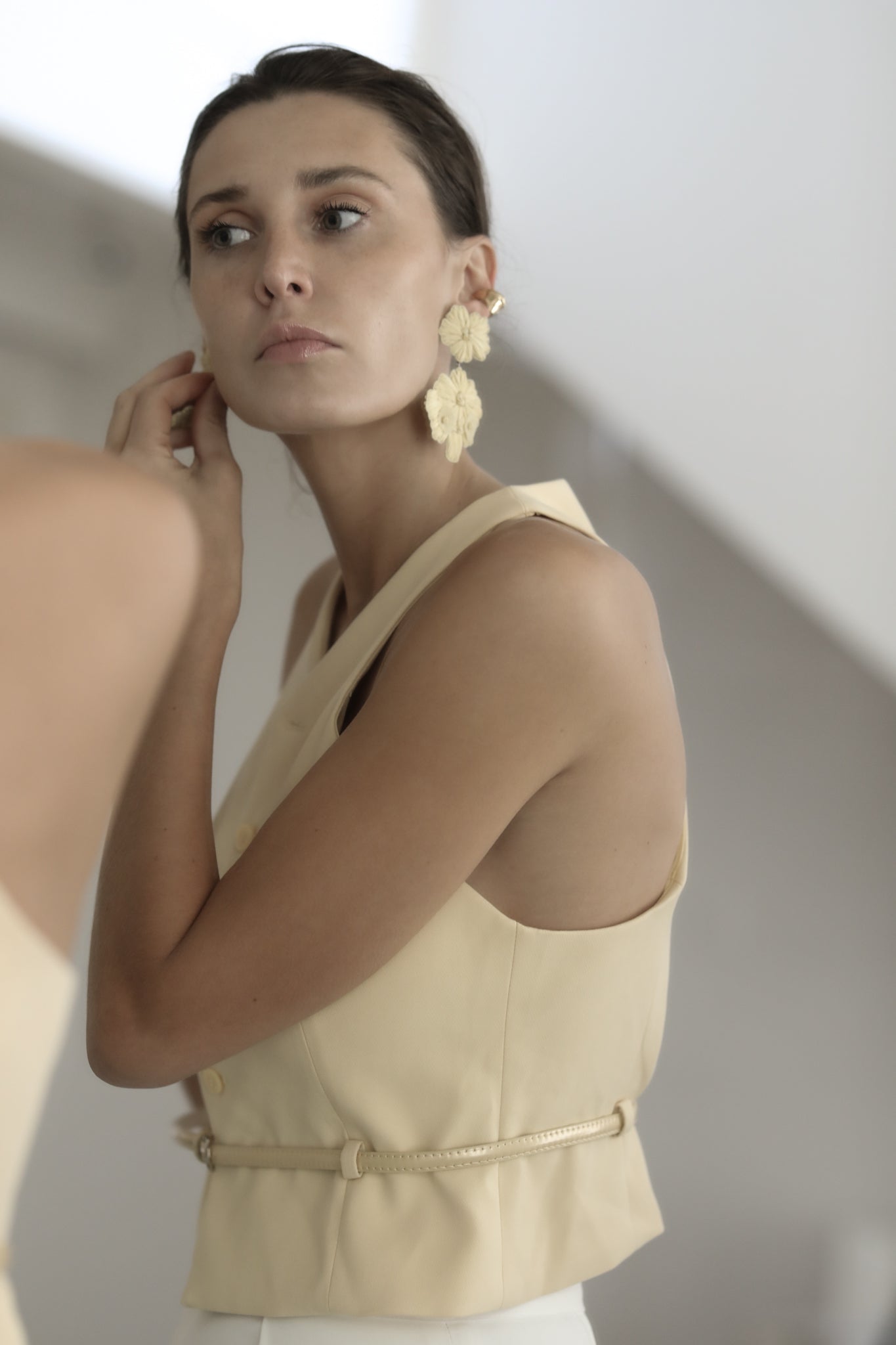 Brunette looking in mirror wearing the Stevie floral statement earrings by AB Ellie paired with butter colored vest