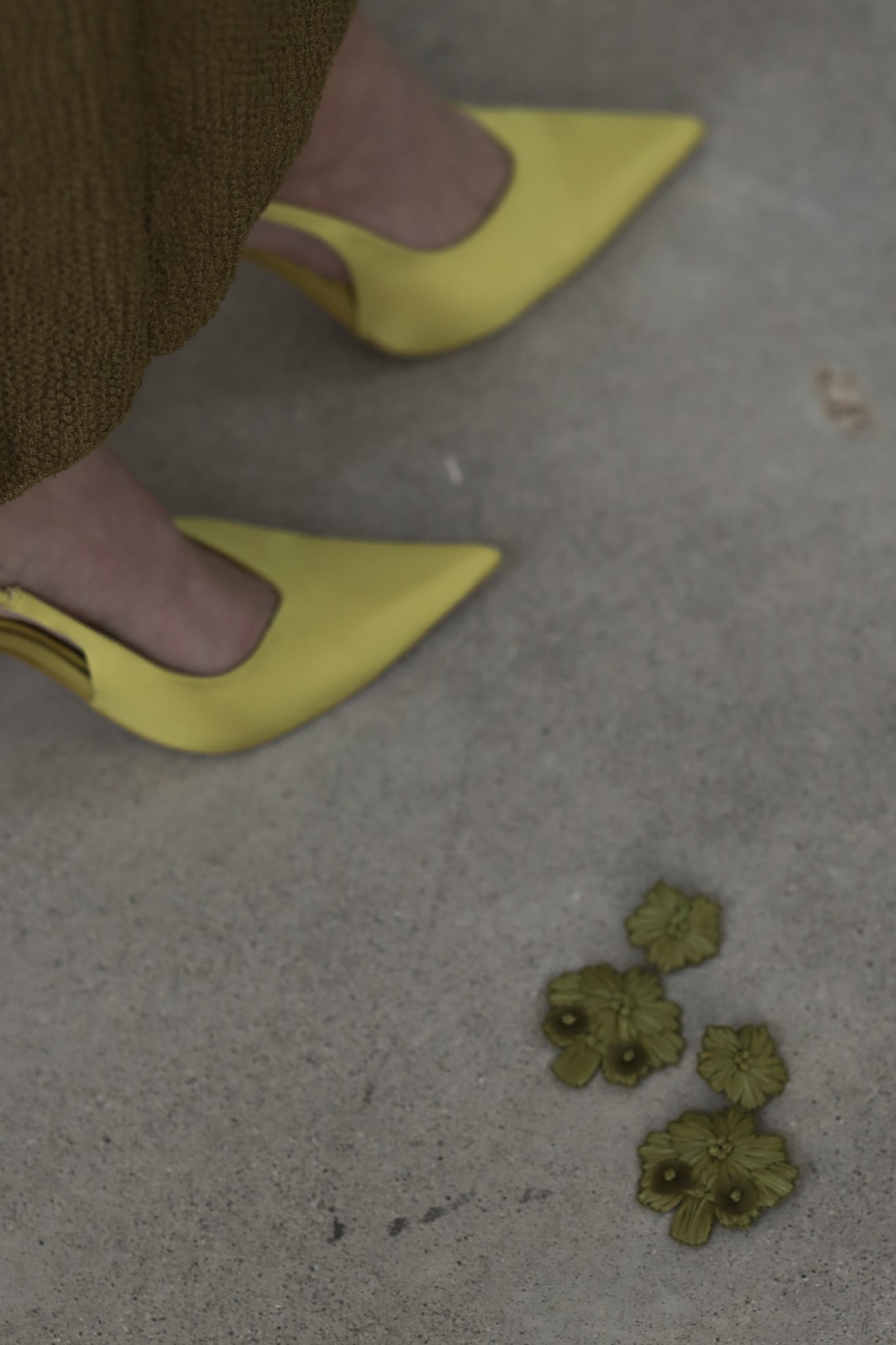 Stevie earrings in olive color laying next to yellow stilettos on concrete floor