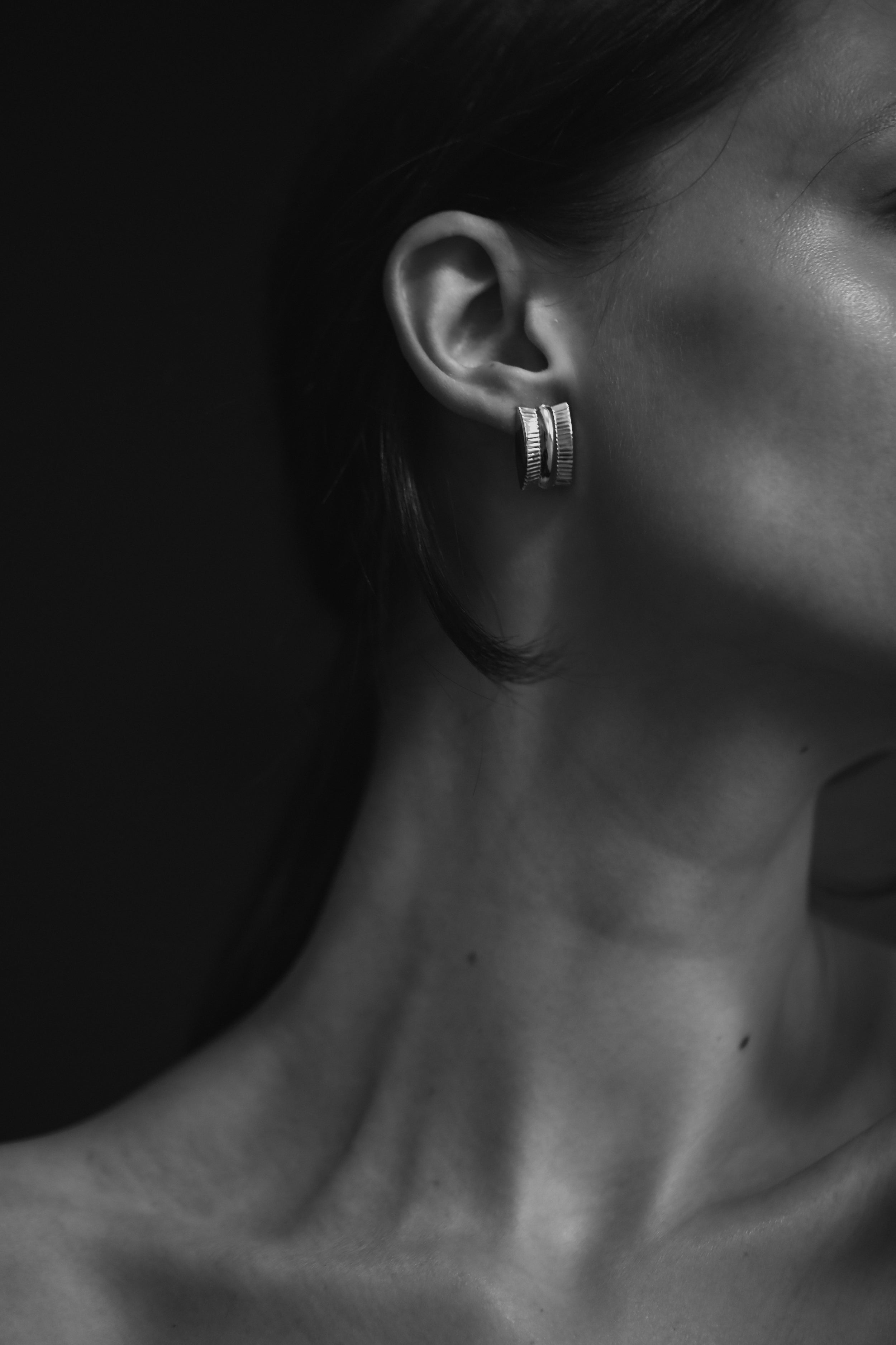 Close-up of brunette woman wearing the AB Ellie Ribbed Channel sterling silver earring against a dark background