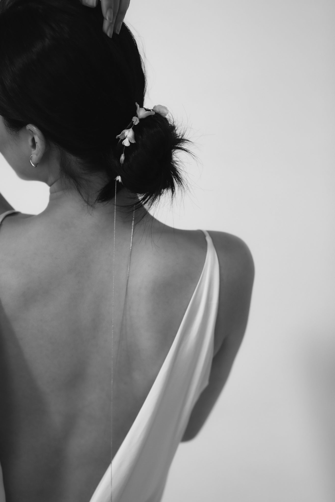 Black and white photo of a bride wearing an open-back dress with a ivory blossom hair wrap on a white background