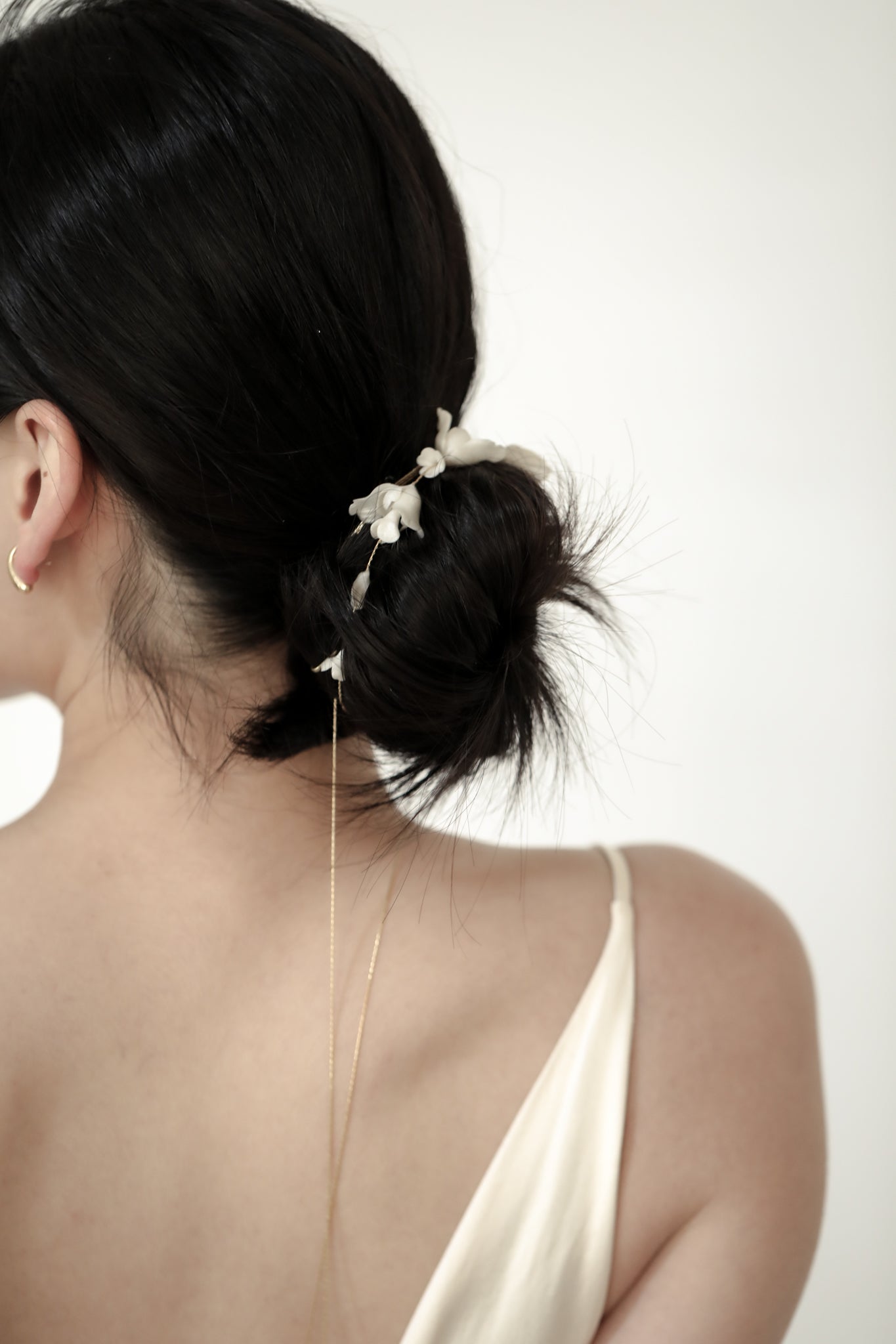 Woman with a stylish hair bun wrapped with the blossom wrap accessory by ab ellie paired with a delicate earring on a white background