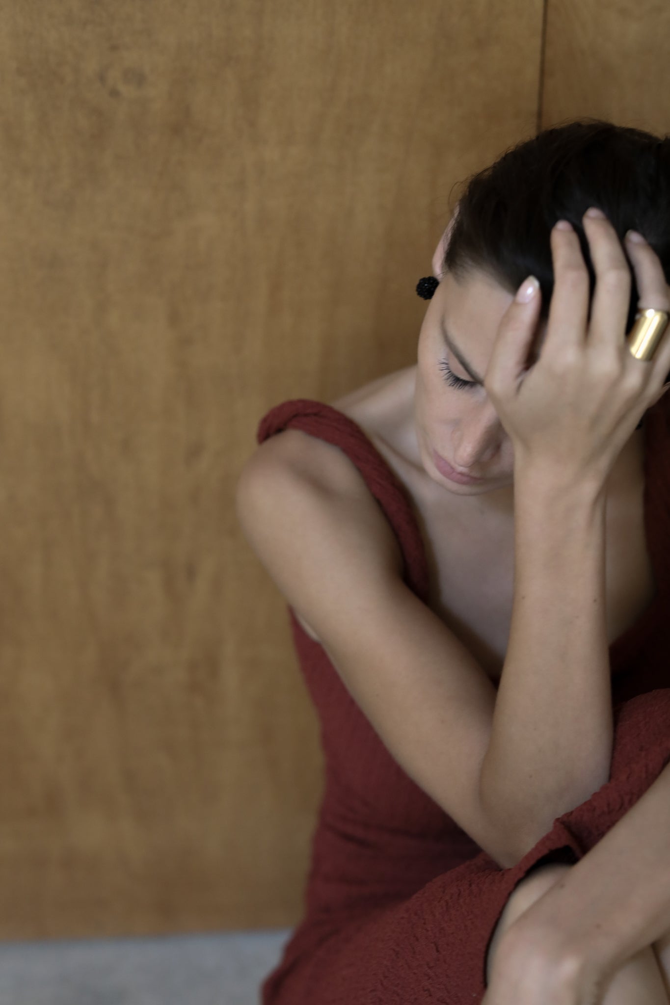 Brunette wearing burgundy dress paired with black Celine studs by A.B. Ellie on wood background