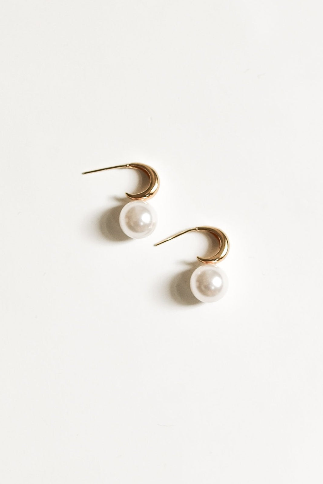 Pair of gold crescent hoop pearl earrings by AB Ellie on a white background