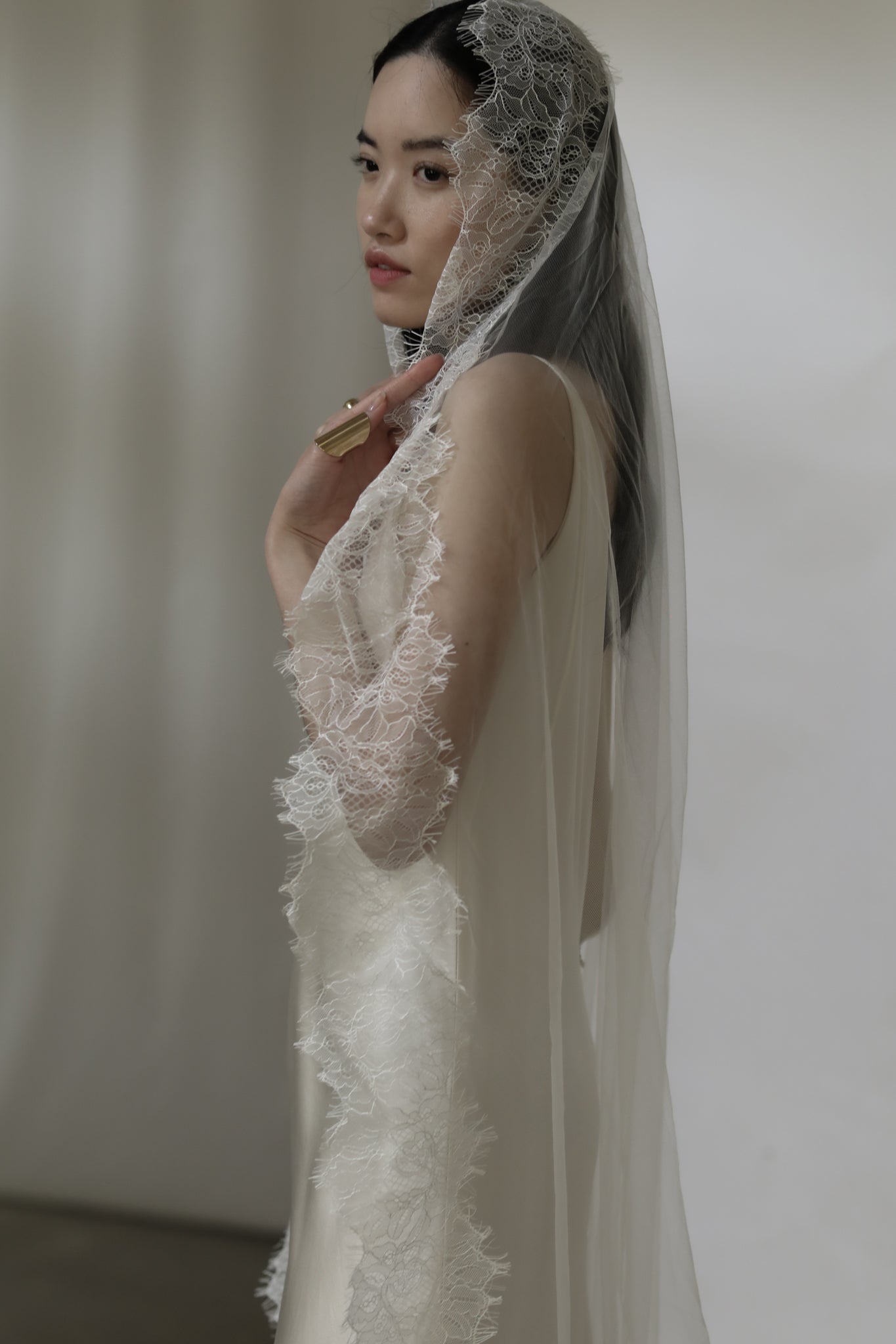 Dark haired bride wearing a lace wedding veil against a white background