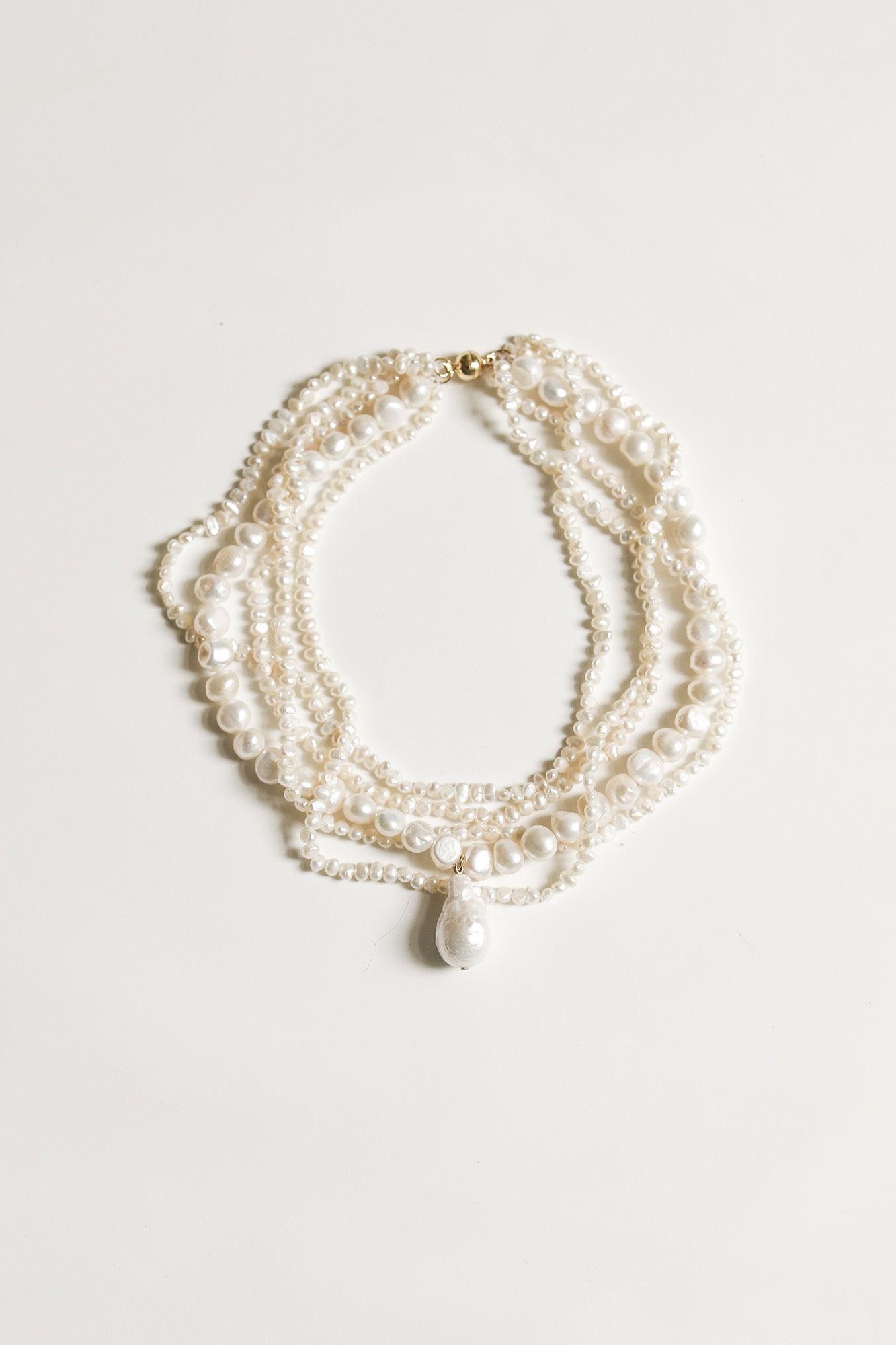 A layered freshwater pearl necklace with a focal drop pearl accent, displayed against a white background.