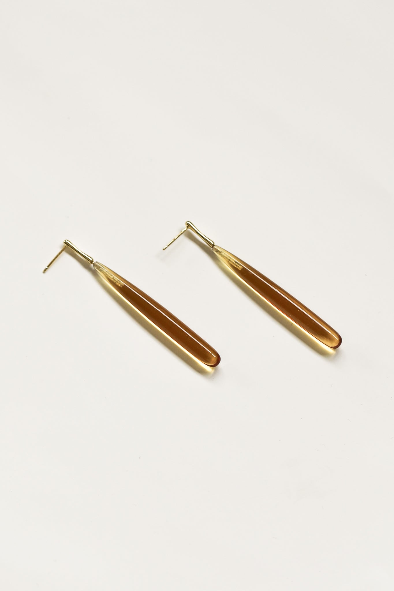 Flat image of svelte glass drop earrings in amber color with gold stem on white background